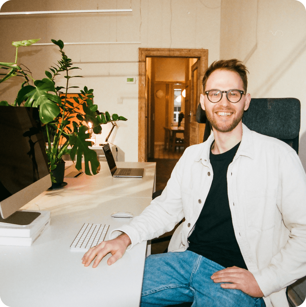 a man wearing glasses sits at a desk with a keyboard