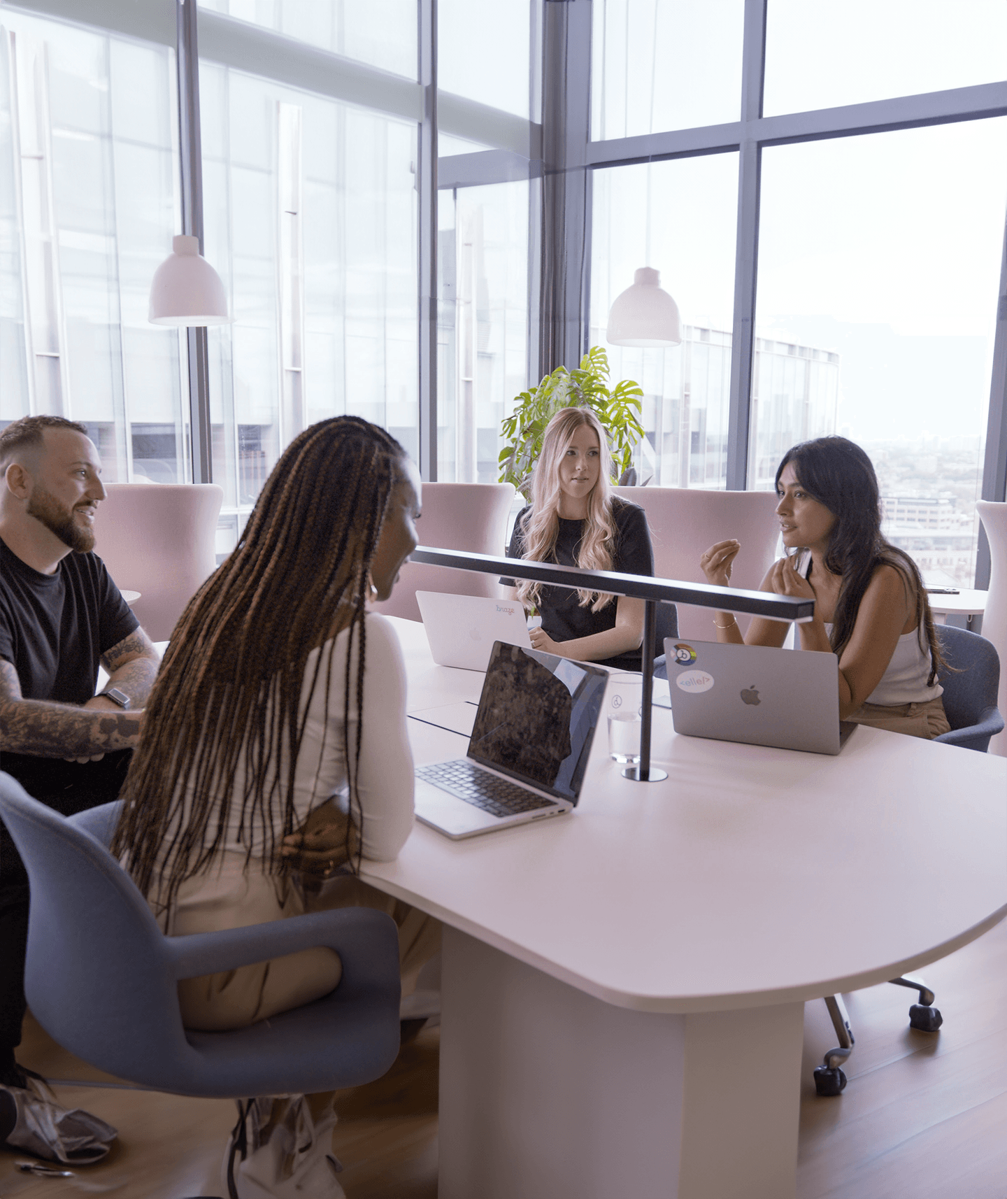 a group of people are sitting around a table with laptops