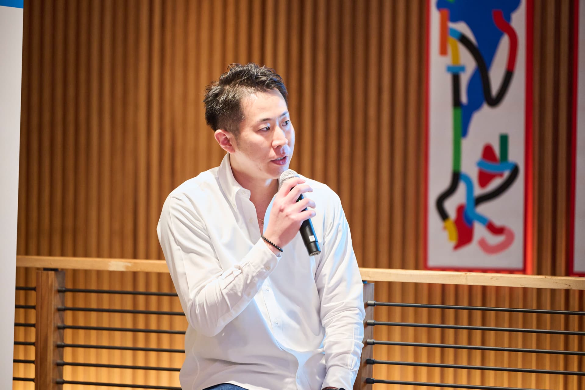 a man in a white shirt is holding a microphone in front of a wooden wall .