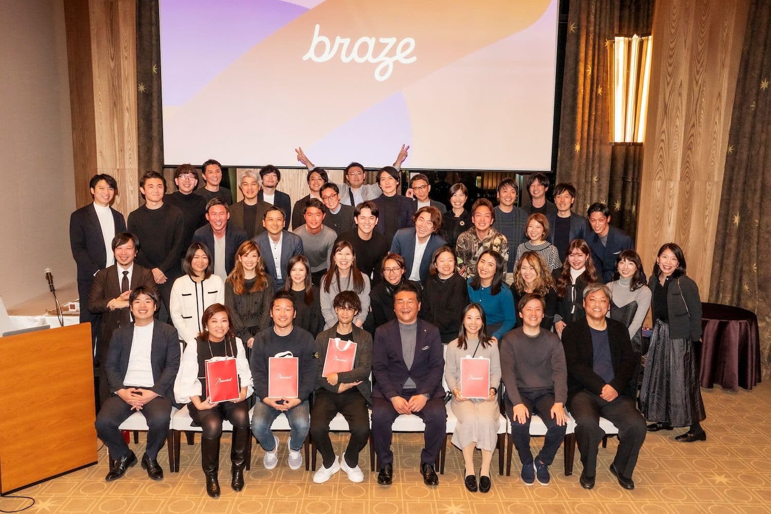 a large group of people are posing for a picture in front of a large screen .