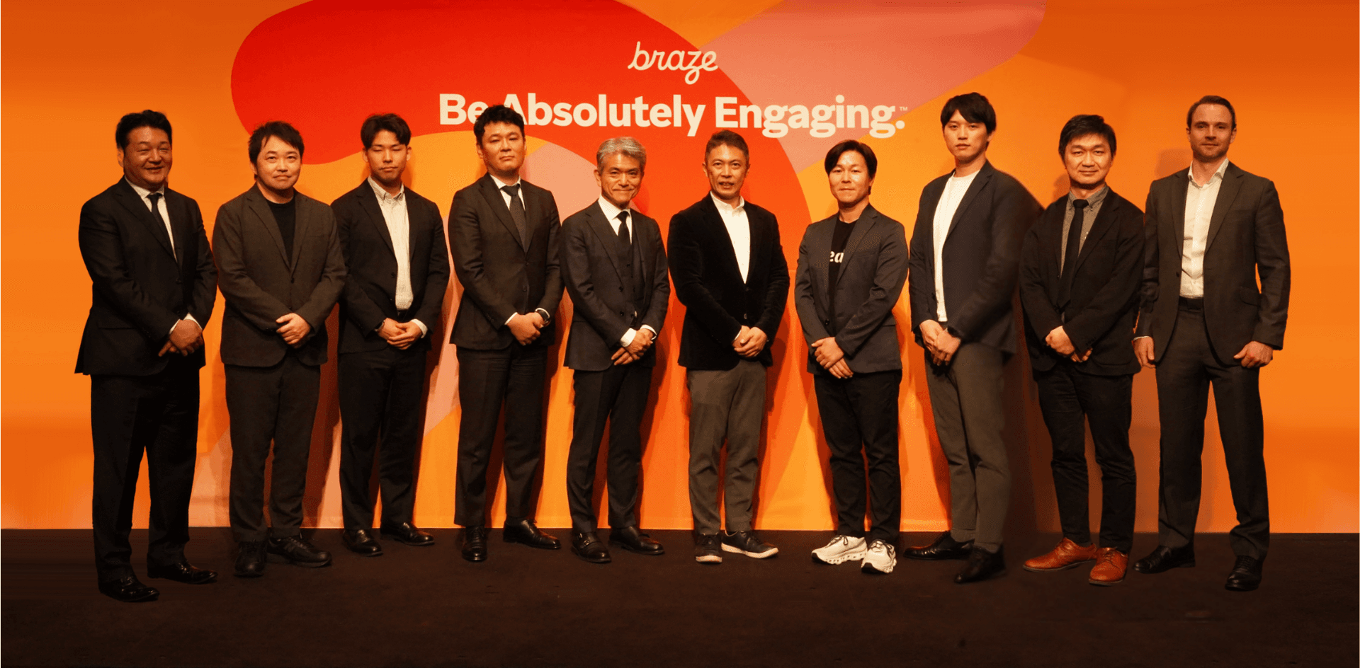 a group of men standing in front of a sign that says braze be absolutely engaging