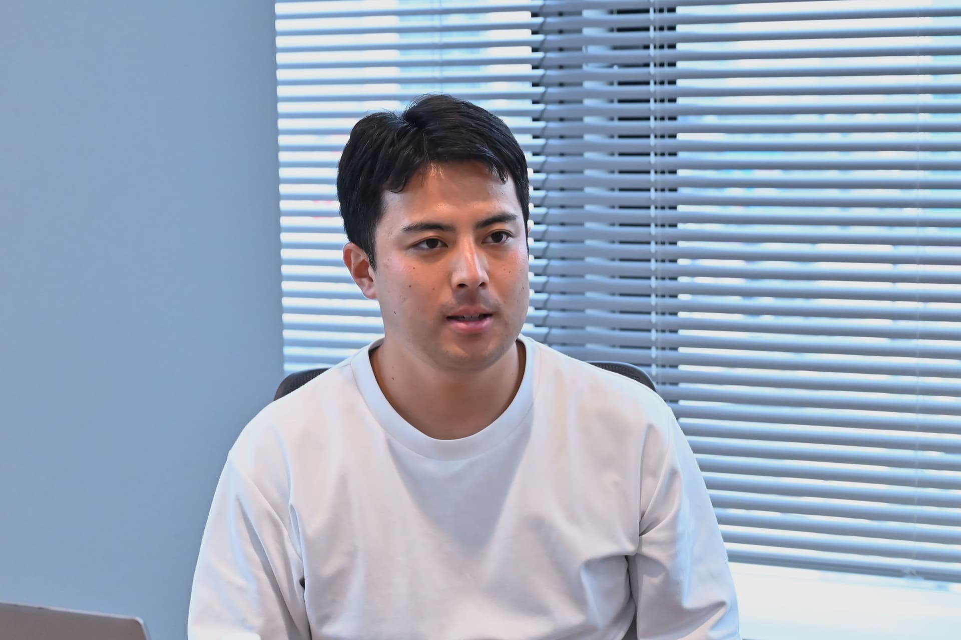 a man in a white shirt is sitting in front of a window with blinds .