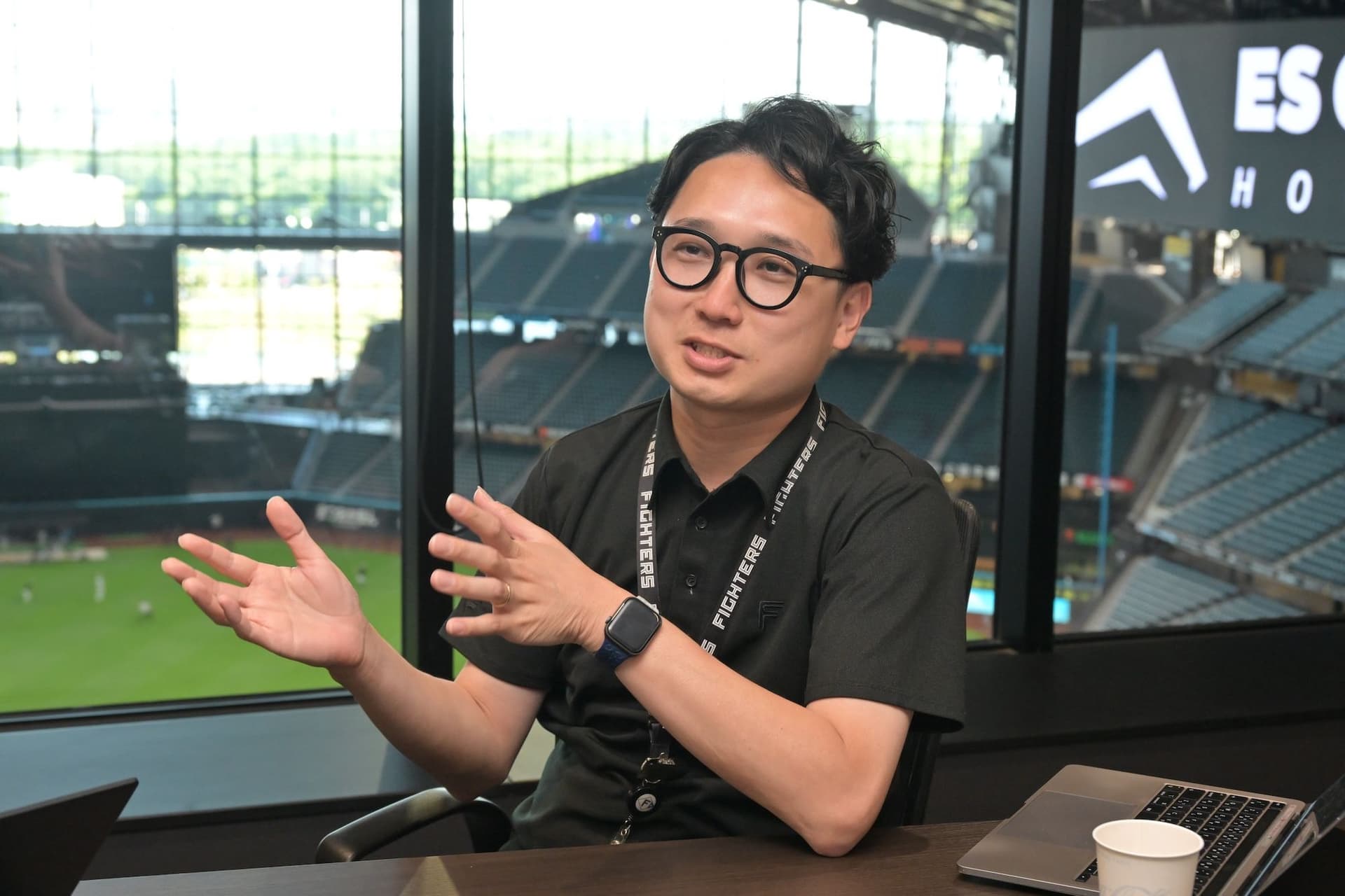 a man wearing glasses is sitting at a table in front of a stadium .