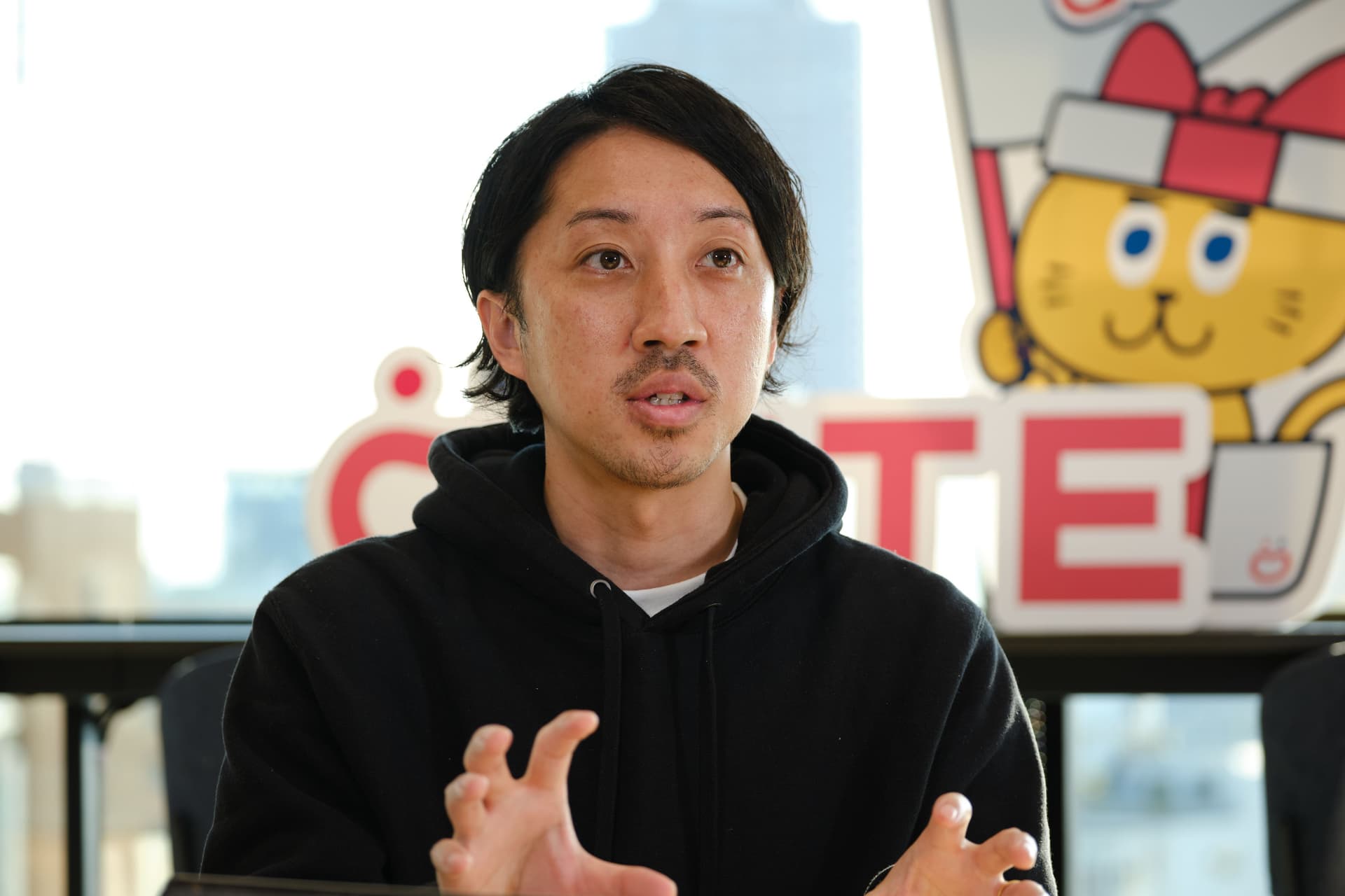 a man in a black hoodie is sitting in front of a sign with a cat on it .