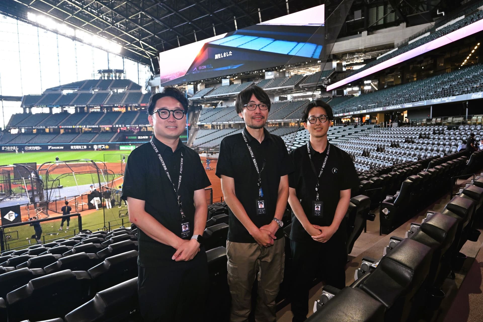 three men are standing in an empty baseball stadium .