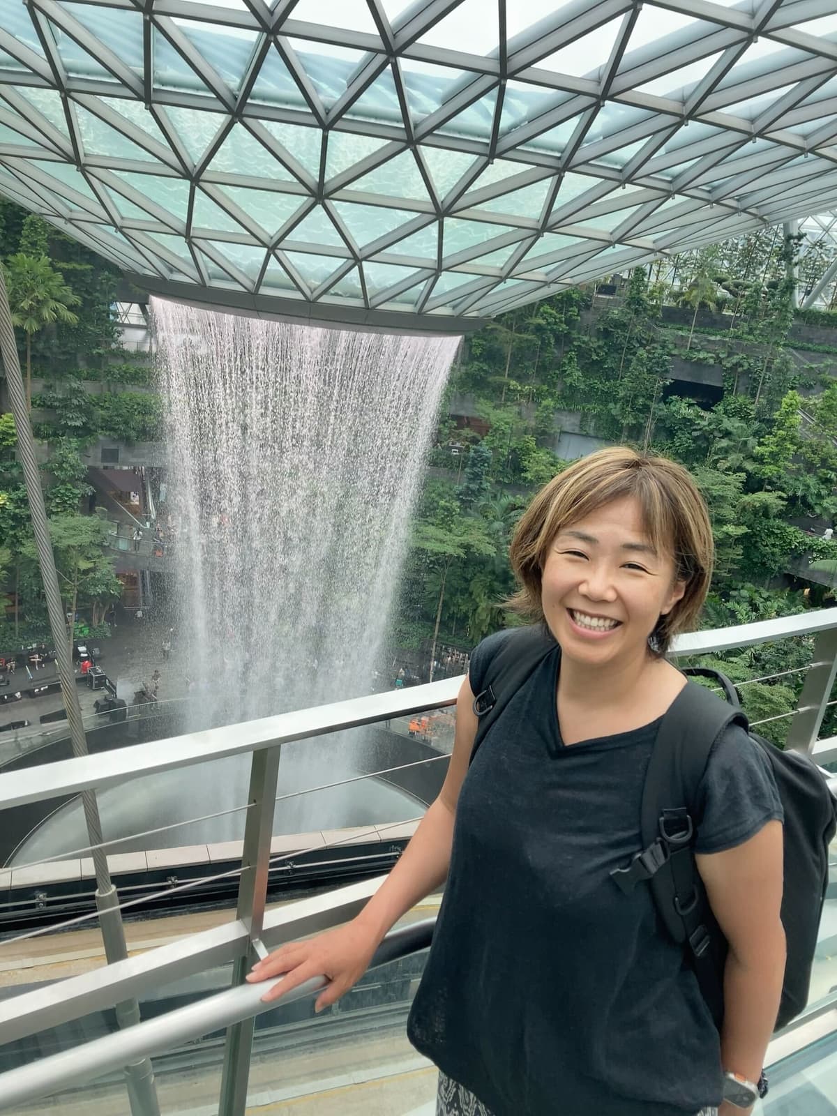 a woman with a backpack is standing in front of a waterfall .