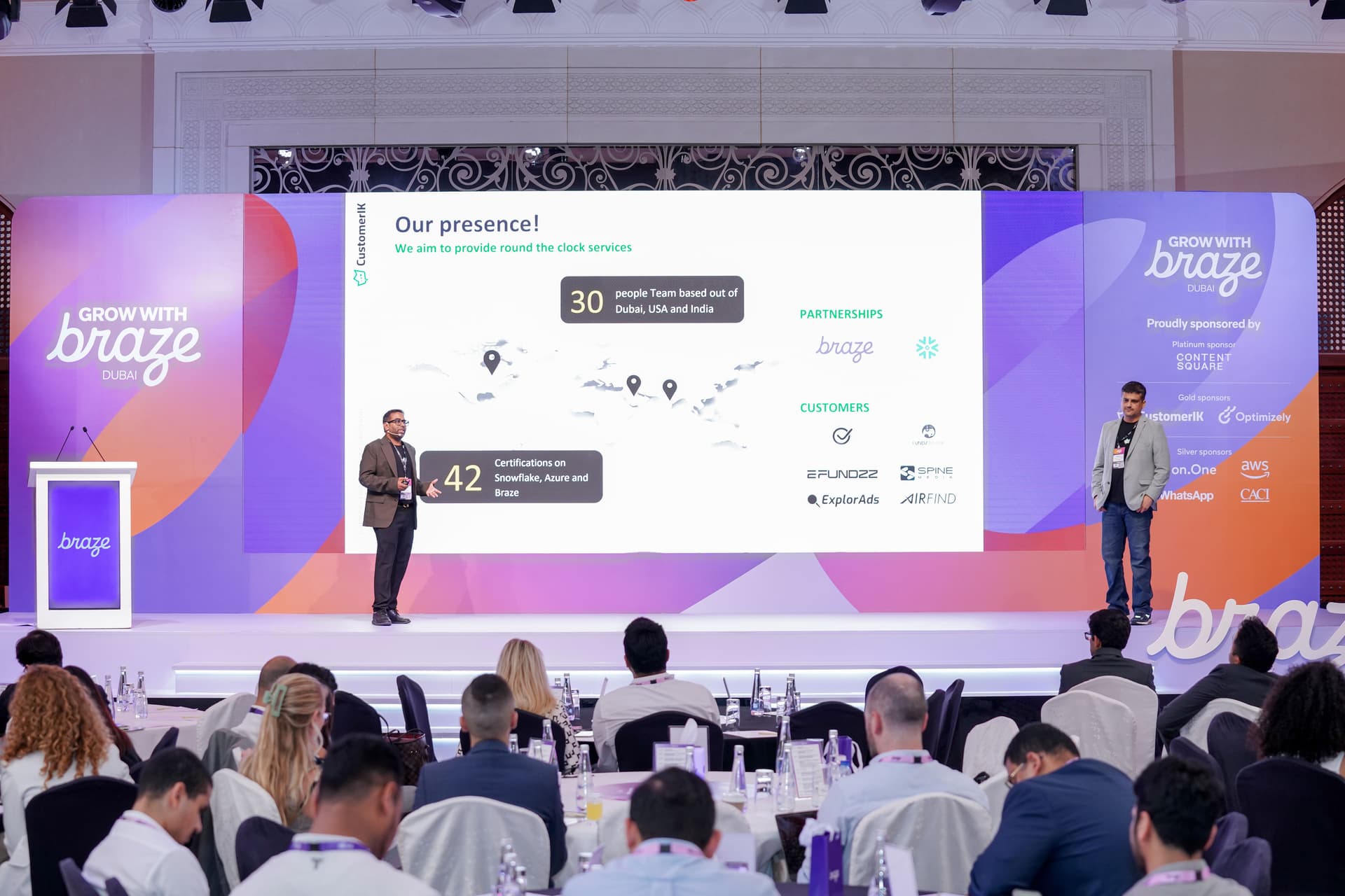 two event speakers presenting on a stage with a screen behind them