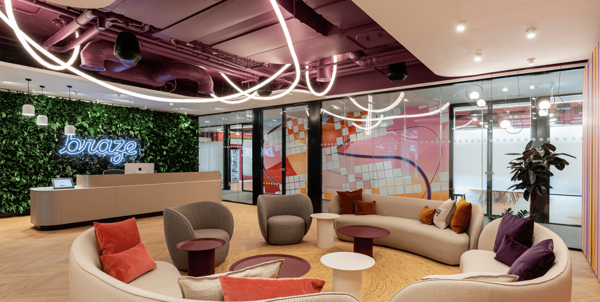 A modern office reception area with a green wall, a neon "braze" sign, and colorful curved seating.