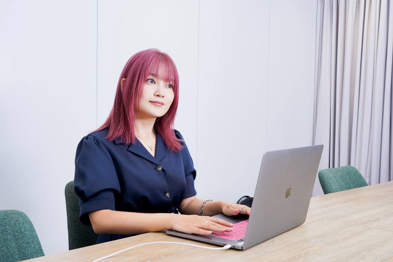 a woman with pink hair is sitting at a table using a laptop computer .