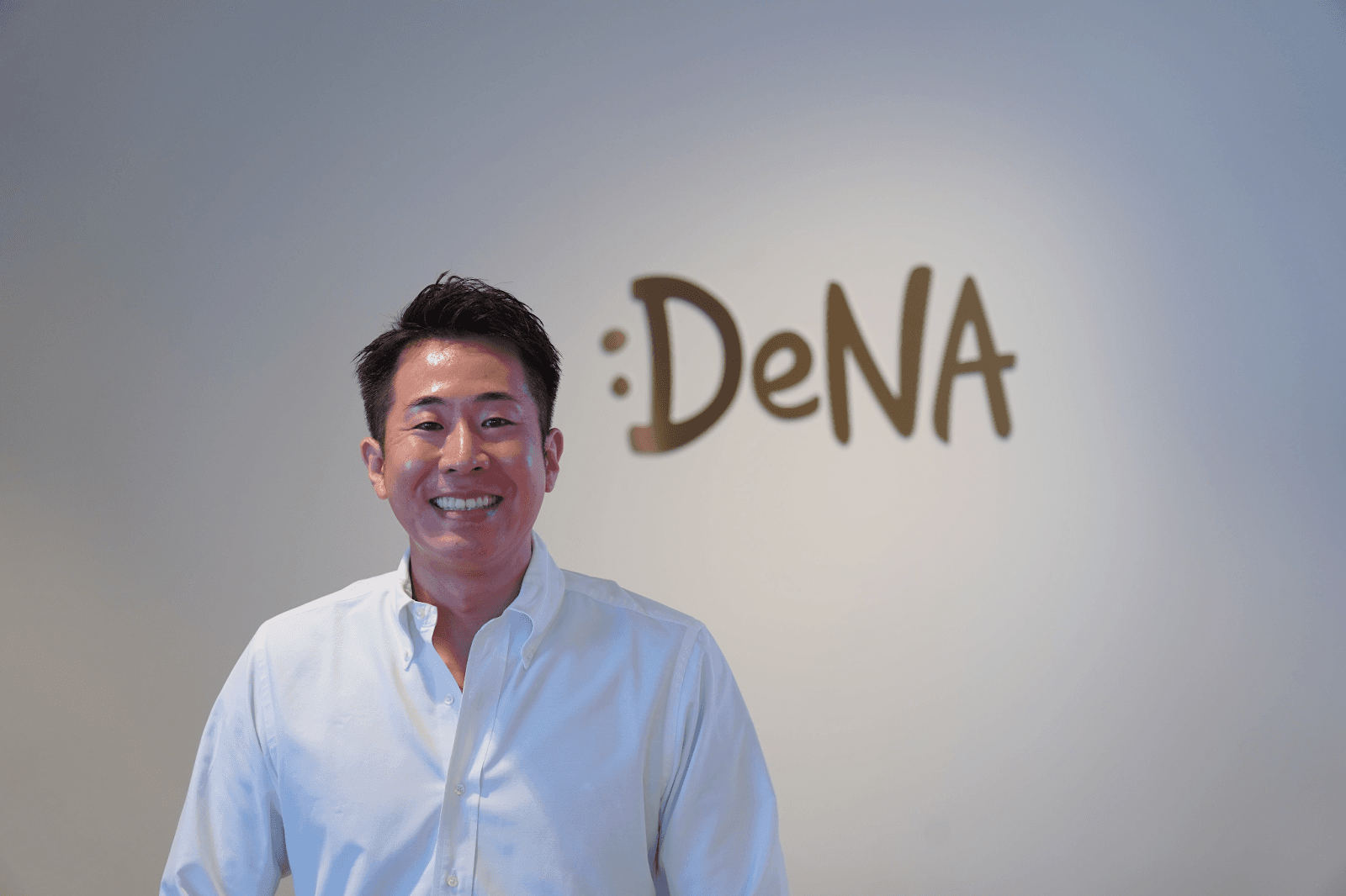 a man smiles in front of a dena sign
