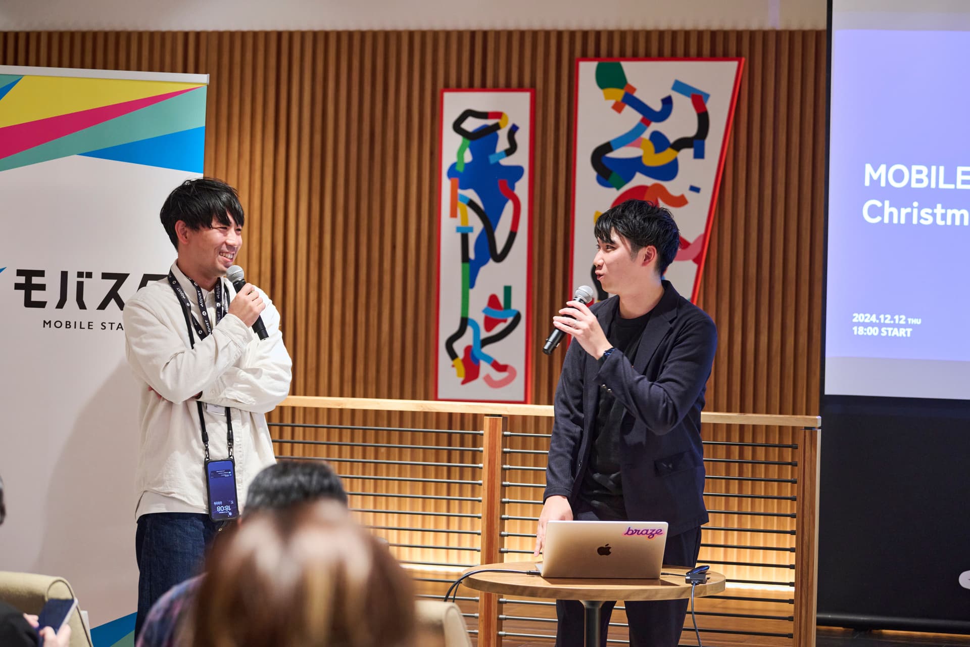 two men are standing next to each other talking into microphones in front of a crowd .