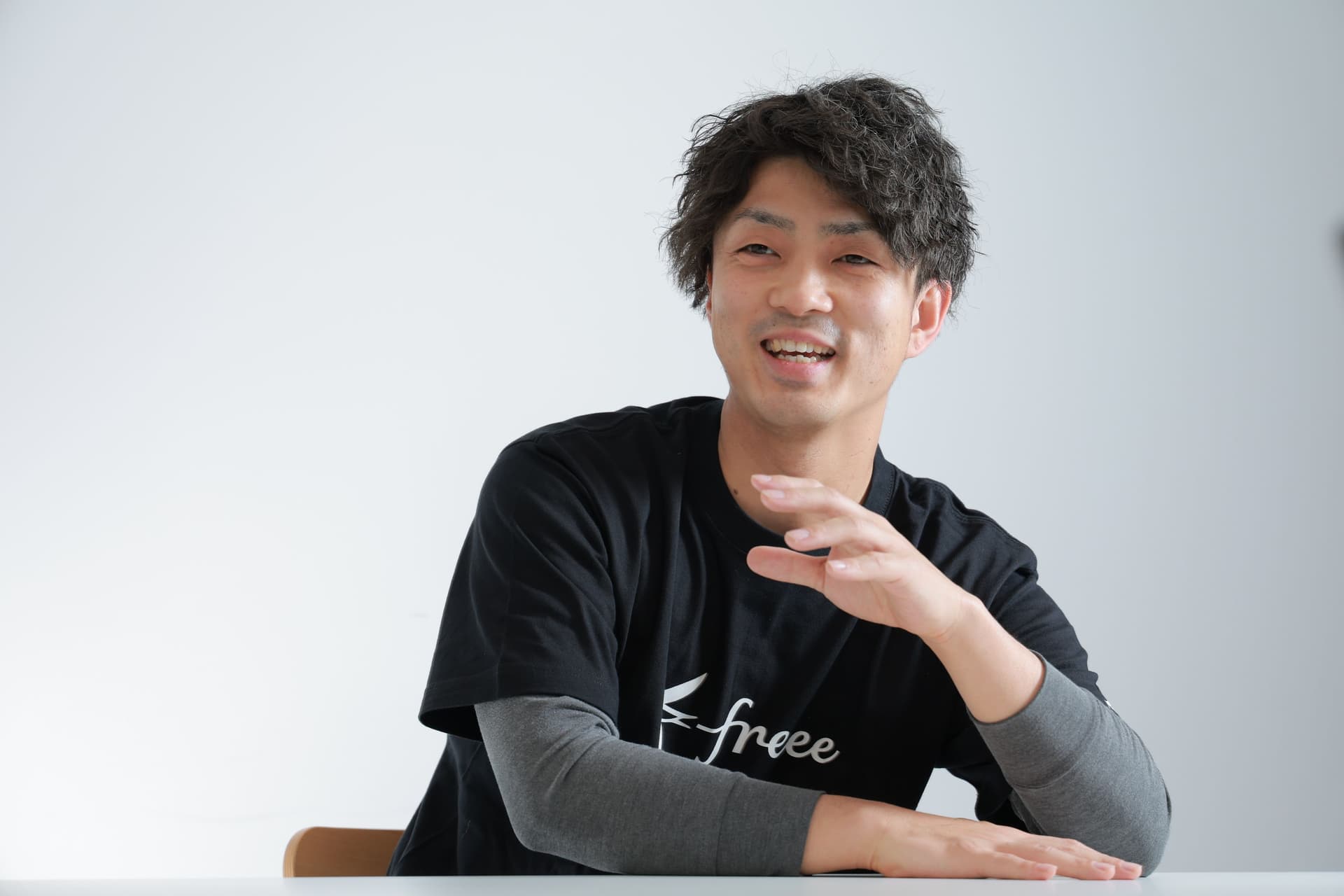 黒く縮れた髪をした男性が、「free」のロゴが入った黒いTシャツを着て、話しながら身振りを交えている。