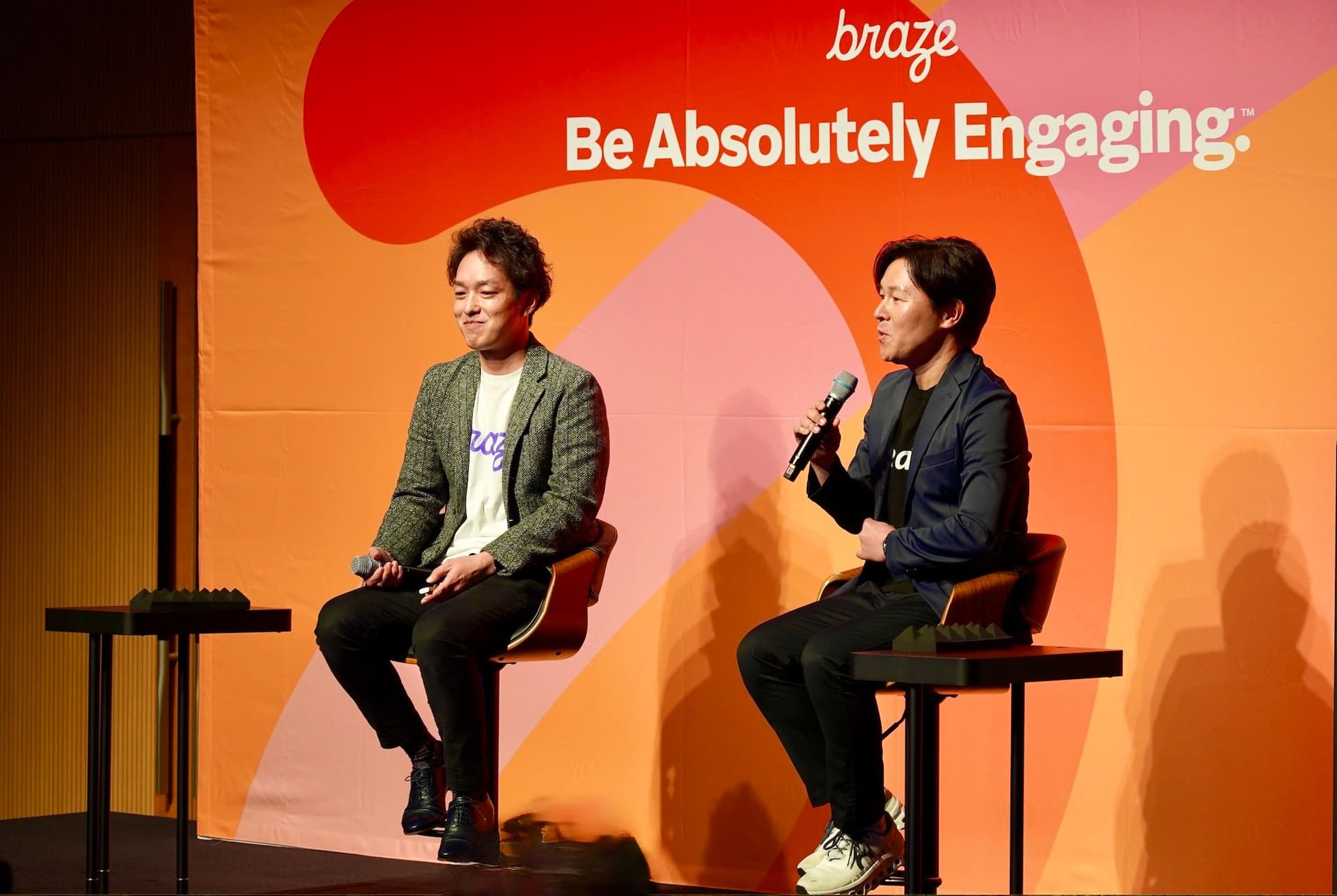 two men are sitting on a stage talking into microphones .