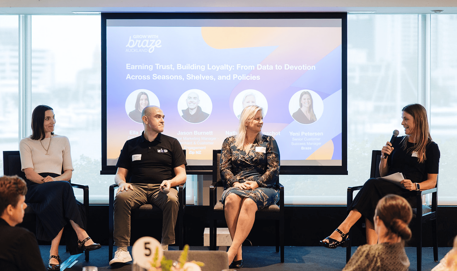 Five people at a panel discussion in front of a screen displaying a presentation on customer loyalty.