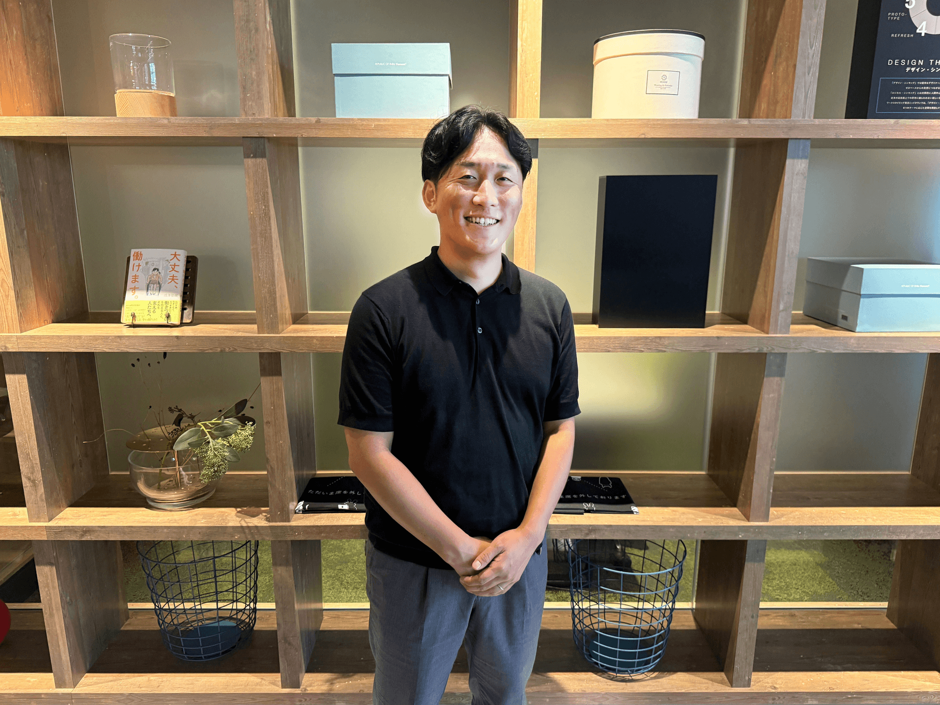 a man in a black shirt stands in front of a shelf with boxes on it