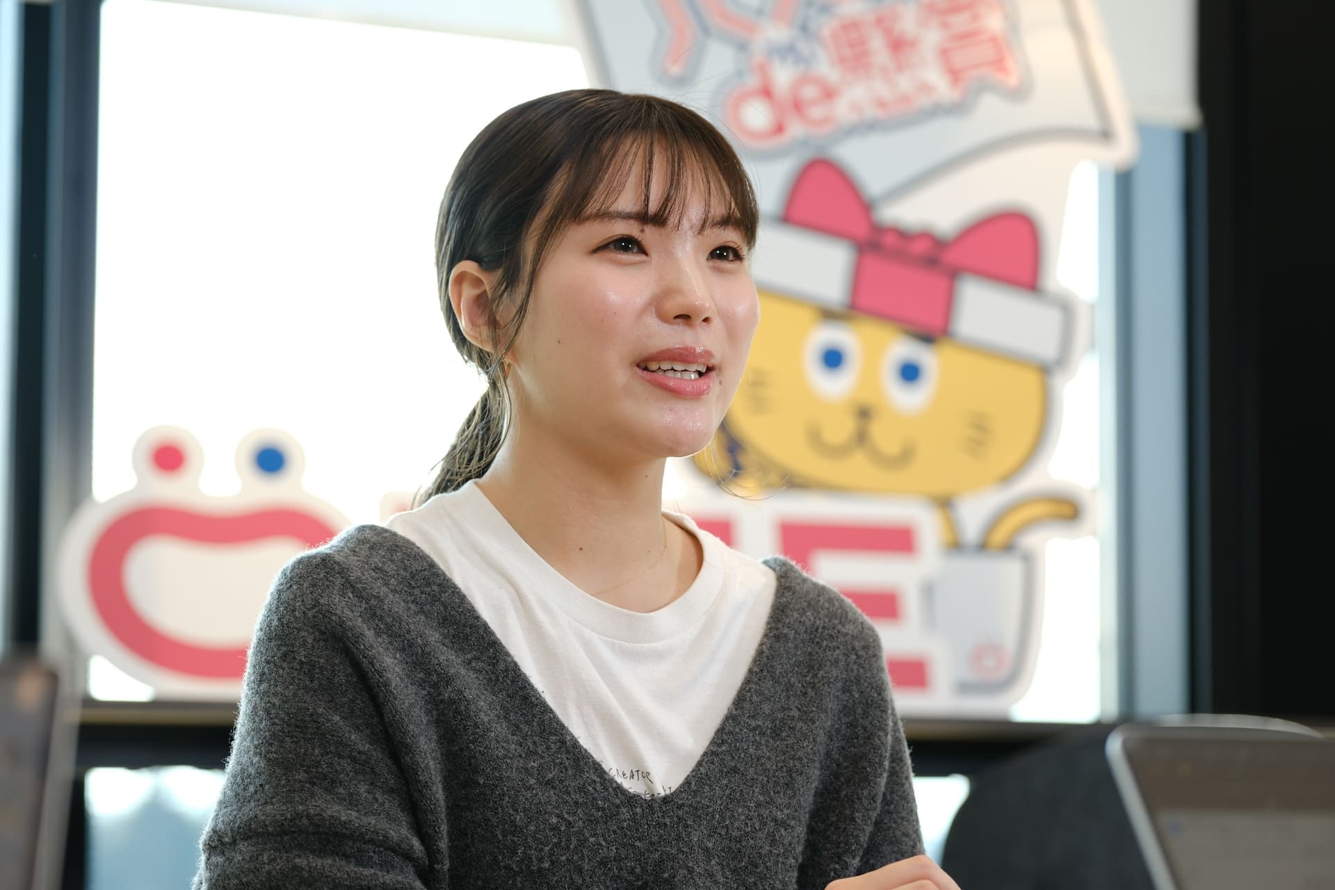 a woman is sitting in front of a window with a cartoon cat in the background .