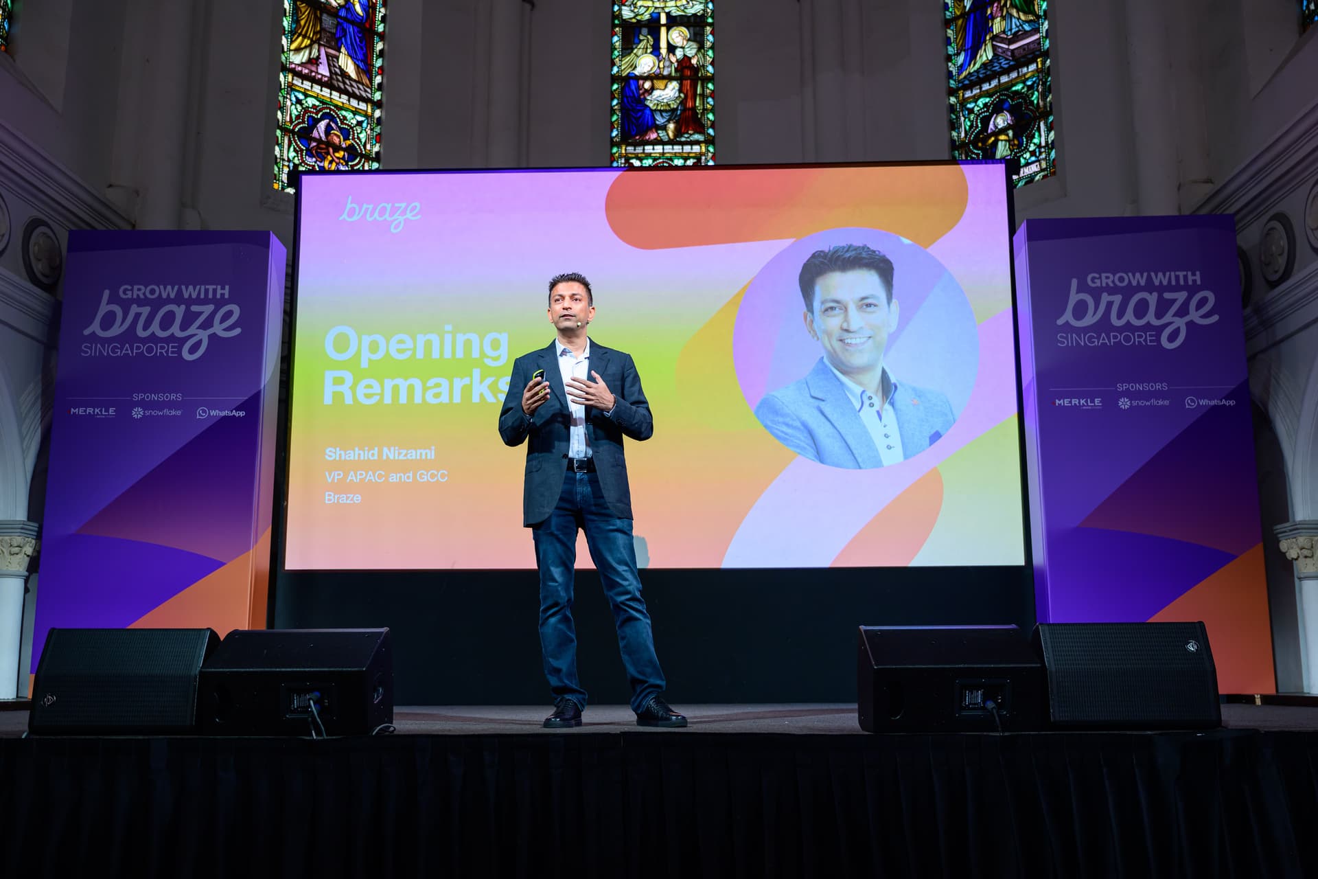 a man is standing on a stage giving a speech in front of a large screen .